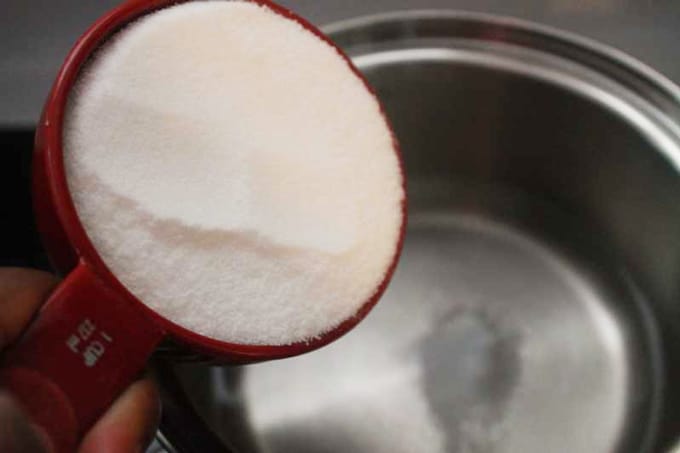 sugar in measuring cup being poured into water in saucepan