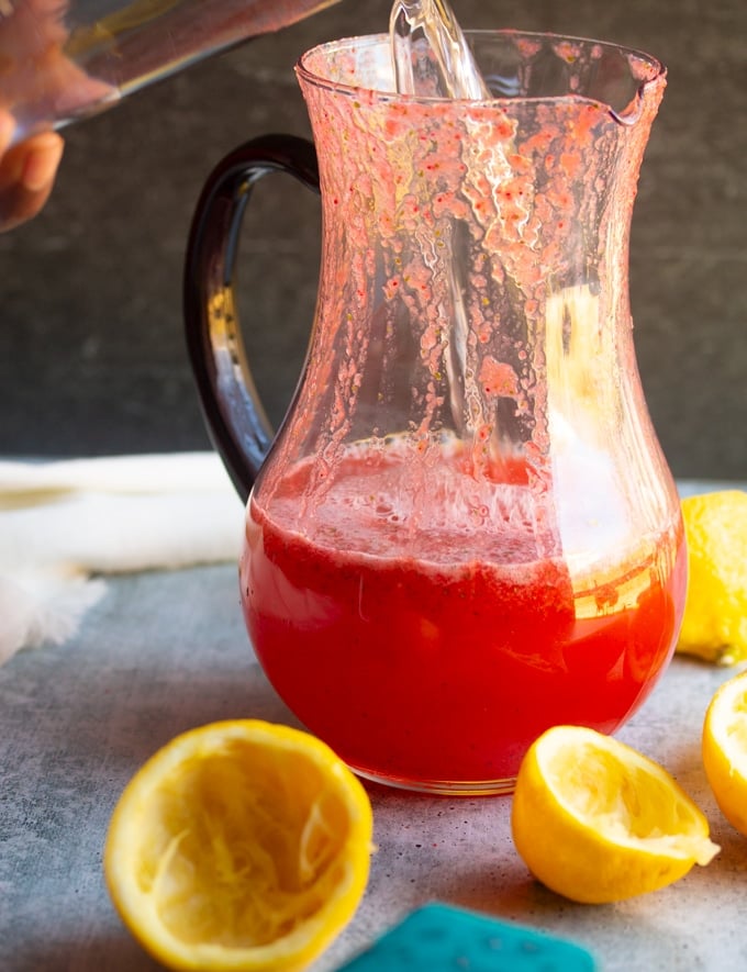 water being poured into pitcher with strawberry syrup