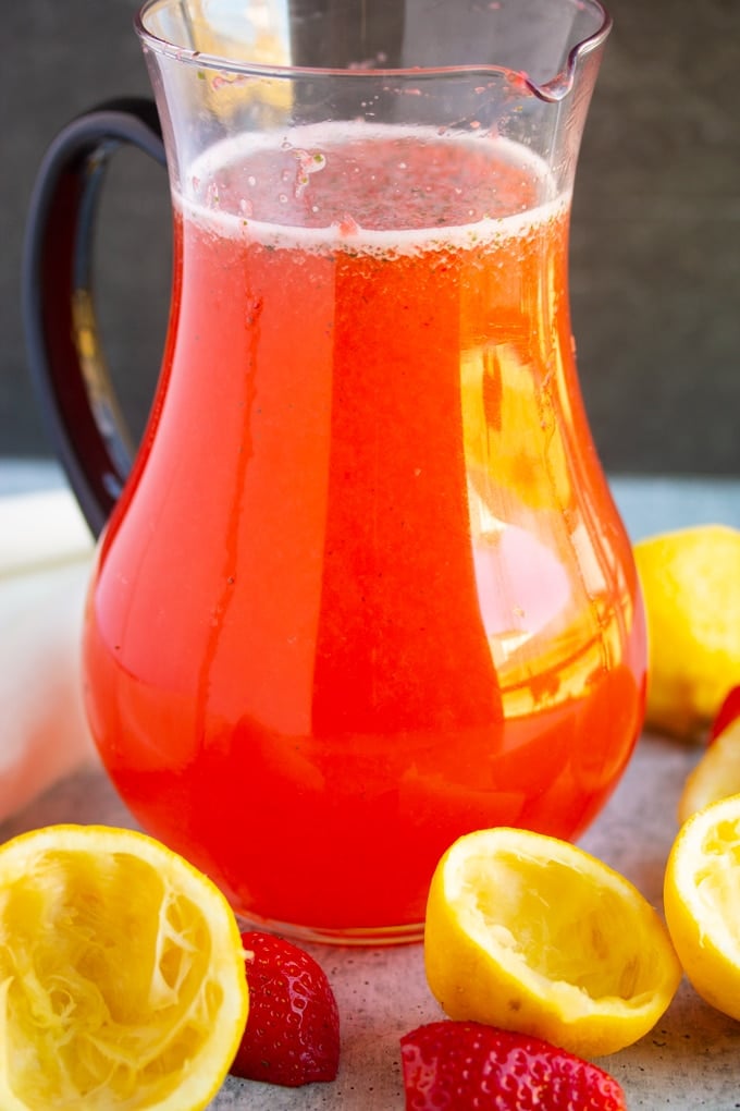 strawberry basil lemonade in a pitcher with lemons surrounding it