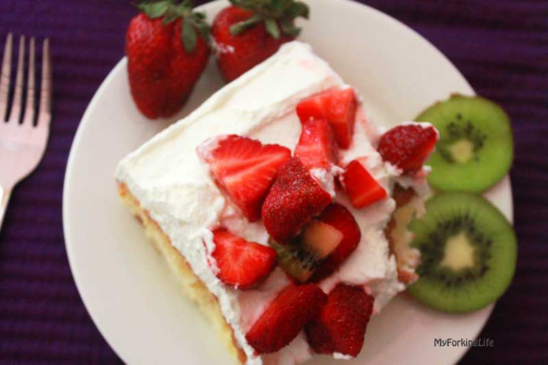 tres leches cake on plate with kiwi and strawberries on top and sides