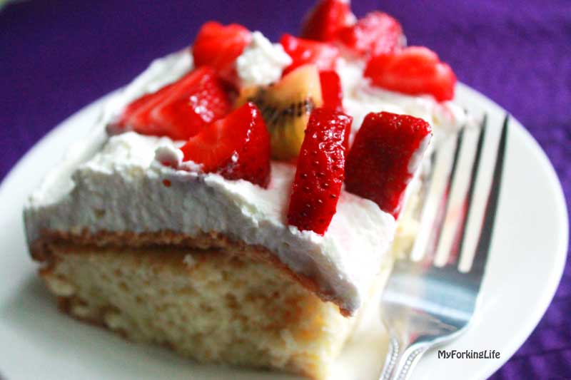 sliced tres leches cake on white plate with fork next to it