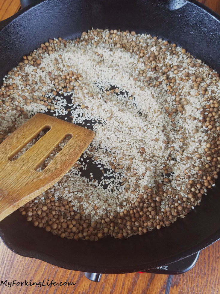 spices being toasted in cast iron skillet with wooden spatula