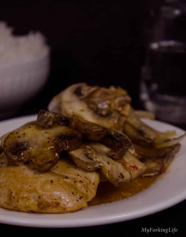 italian baked chicken and mushrooms on a plate with dark background