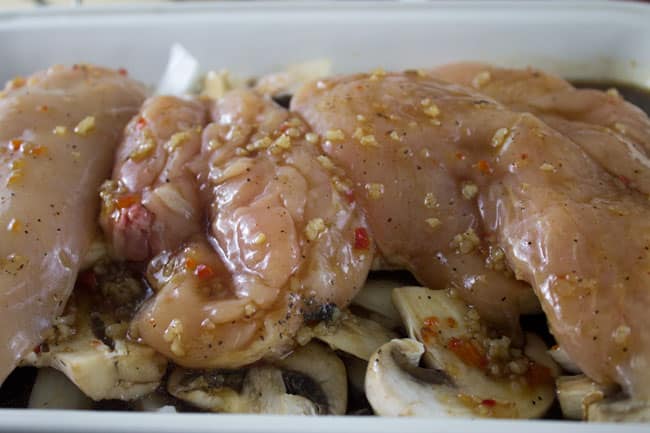 raw chicken on mushrooms in white baking pan