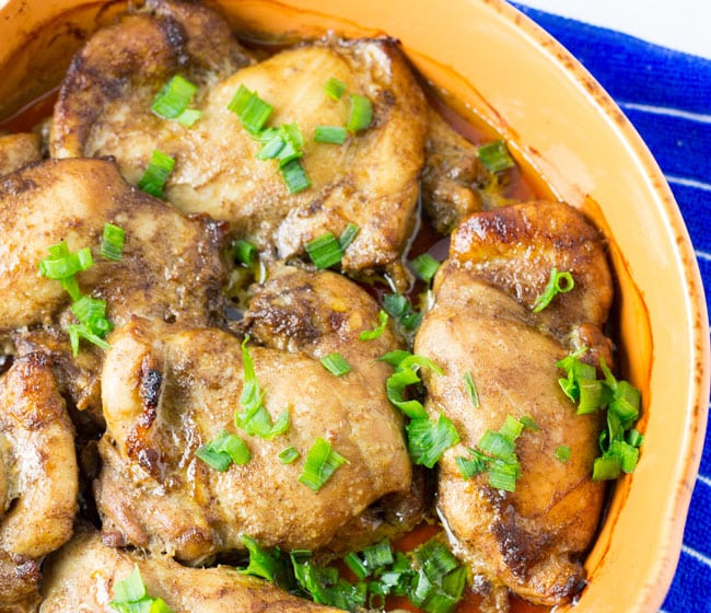 five spice chicken thighs covered in green onion in orange plate