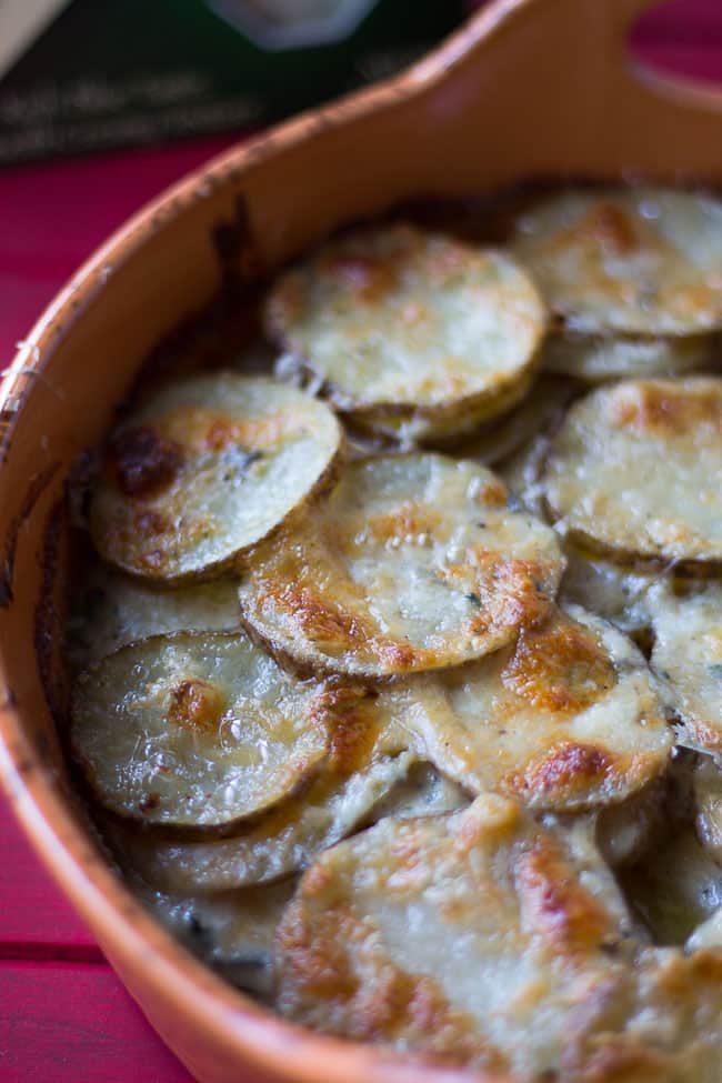 scalloped potaoes covered in blue cheese in orange baking dish