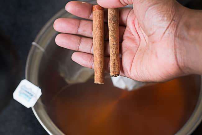 cinnamon sticks in hand over saucepan