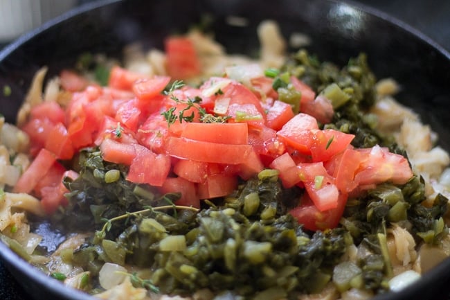 tomatoes added to cast iron skillet with callaloo and saltfish