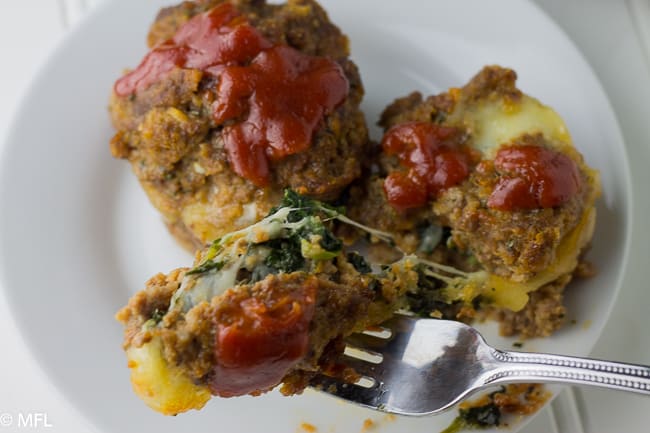 fork picking up piece of stuffed meatloaf with spinach on white plate