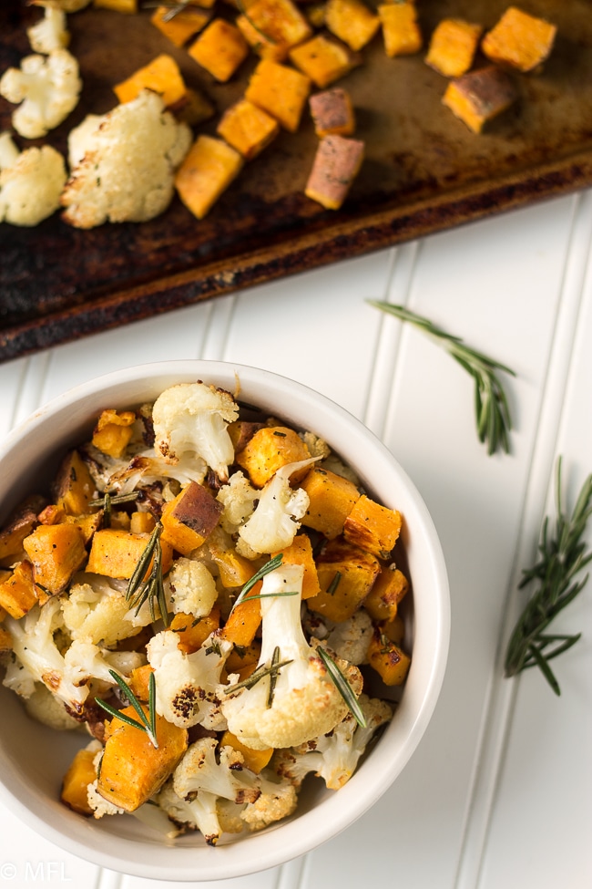 roasted cauliflower and sweet potato in white bowl with rosemary springs on top and side