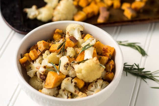 cooked cauliflower, sweet potato, and rosemary in white bowl with baking sheet in background