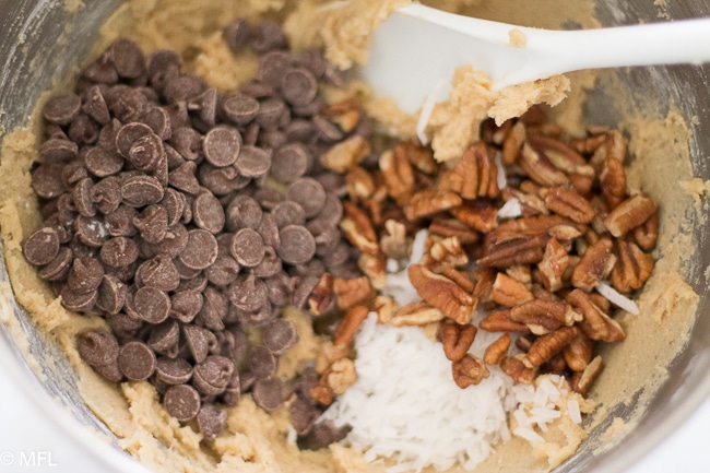 ingredients for chocolate chip pecan cookies in steel bowl with white spoon sticking out