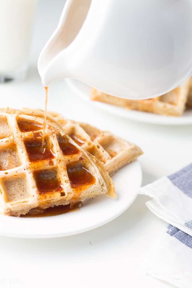 syrup being poured on waffle on white plate