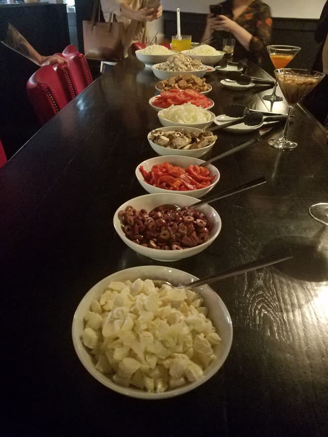 pizza toppings in white bowls on top of long wooden table