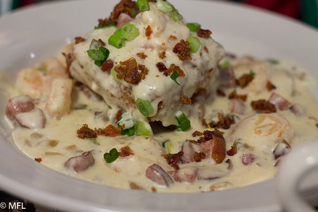 grit cake covered with gravy and bacon and green onions on white plate