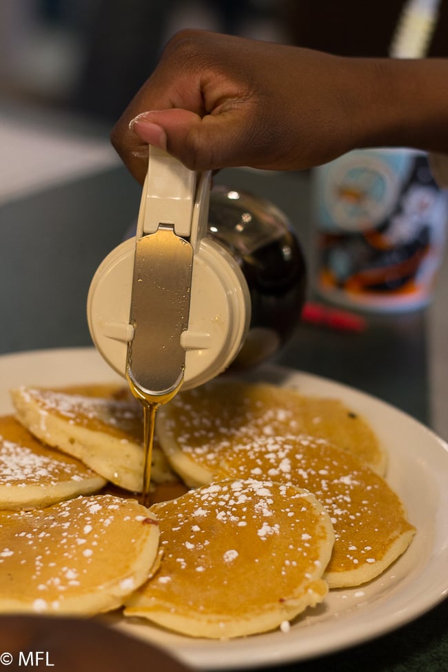 hand pouring syrup over pancakes