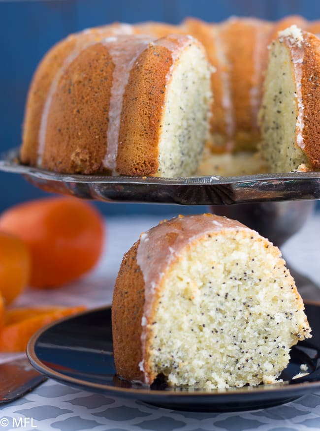 orange poppyseed bundt cake on cake pan with cake slice at bottom