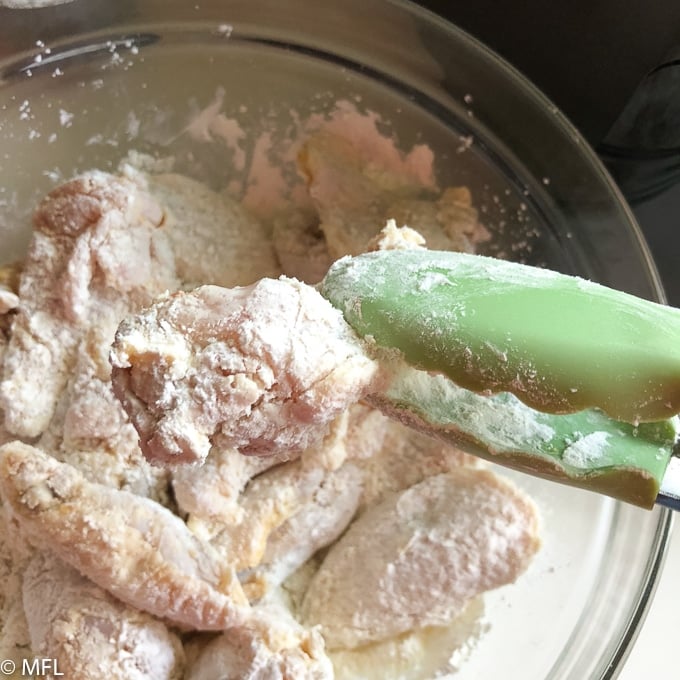 tongs picking up chicken shaking off excess cornstarch