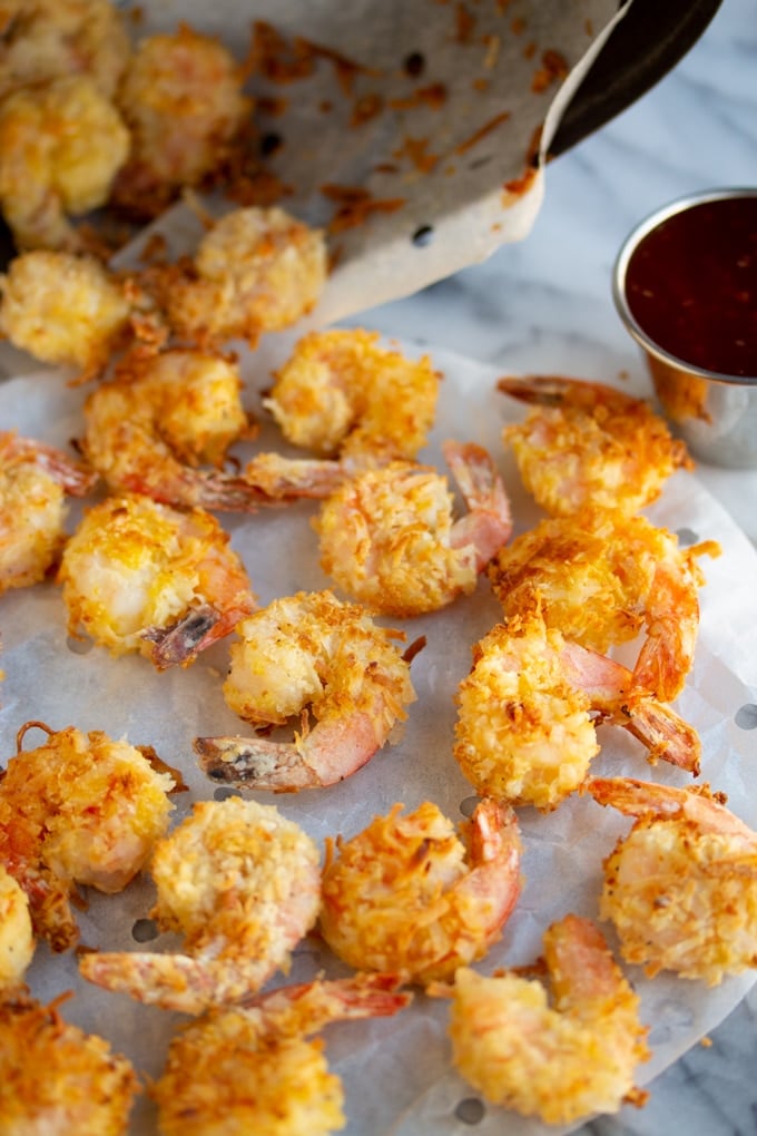 These Crispy Coconut Air Fried Shrimp are covered in a delicious crispy coconut breading. Pair them with your favorite thai chili sauce for the perfect flavor combination. #airfryerrecipe #airfryershrimp #crispycoconutshrimp air fryer shrimp with coconut breading on a table