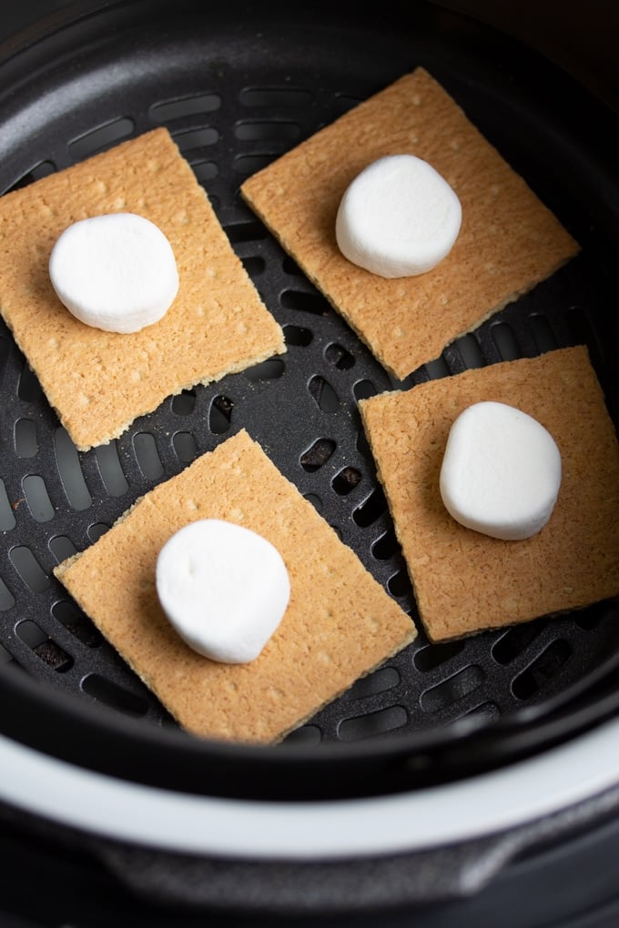 You won’t need a campfire to make these s’mores, all you need is an Air Fryer. Delicious roasted marshmallows roasted right in the Air Fryer in less than 10 minutes. It’s the perfect easy dessert. #smallbatchdessert #airfryer #airfryerrecipes #airfryerrecipesfordessert #dessertrecipes graham crackers with marshmallows on top in air fryer