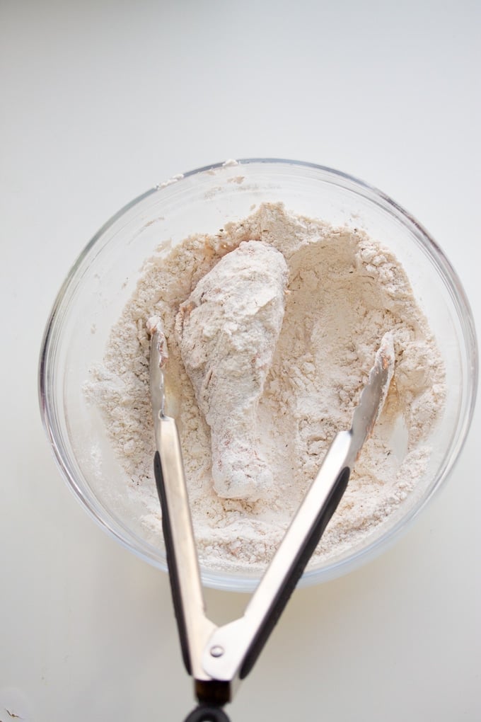 chicken leg in flour with tongs 