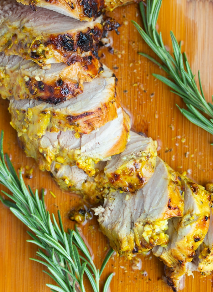air fryer pork tenderloin sliced on a cutting board with rosemary springs on the side