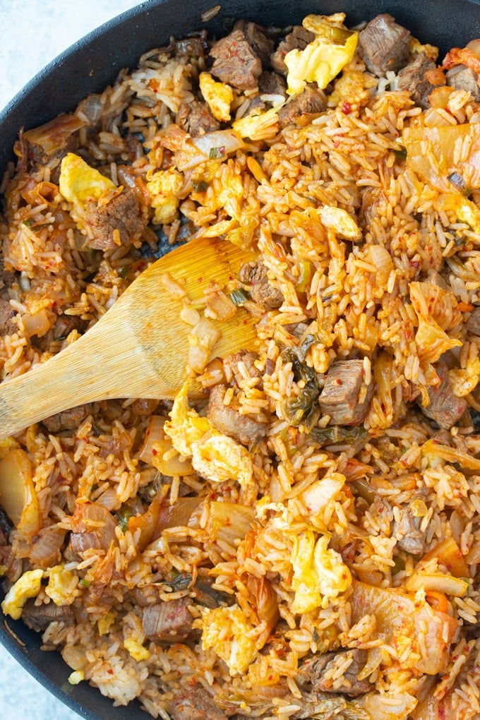 steak kimchi fried rice in a skillet with wooden spatula sticking out