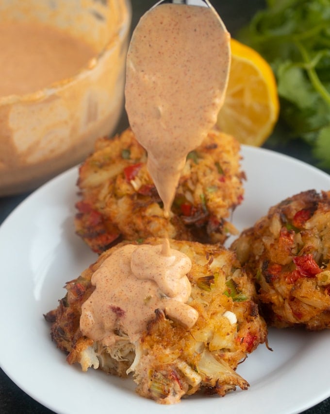 crab cakes on white plate with sauce being poured on top