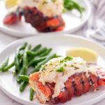 cooked lobster tails on white plate with green beans in background