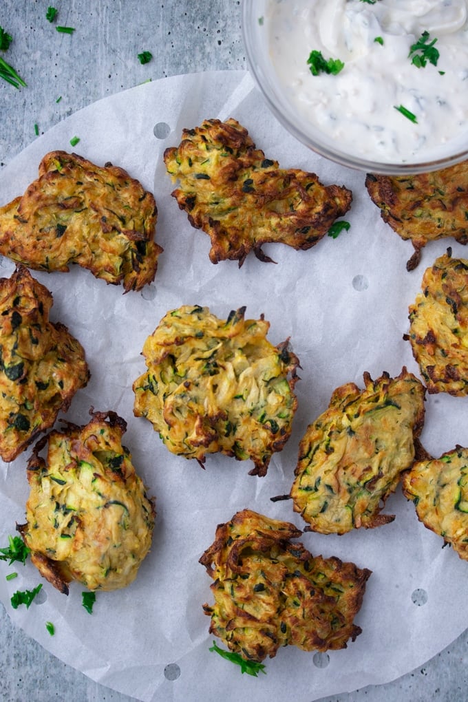 air fryer zucchini fritters laid out on parchment paper with dipping sauce on the side