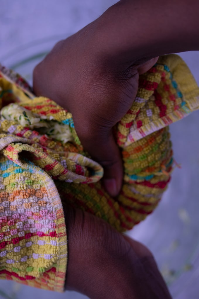 hands squeezing zucchini with yellow dish towel 