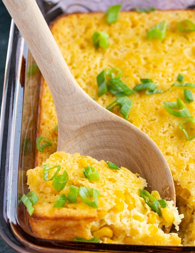 corn souffle with green onions on top with spoon sticking out