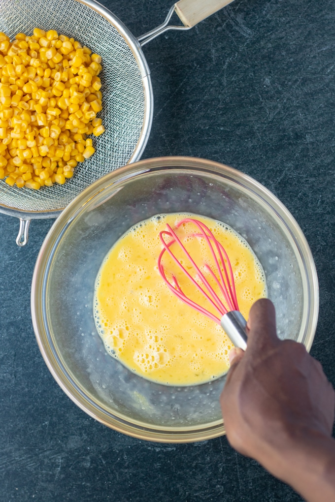 eggs being whisked in bowl with corn on the side in a strainer