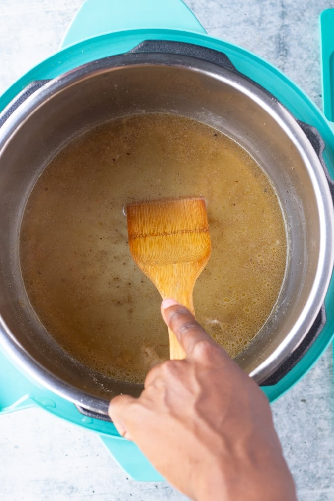 hand using wooden spoon to stir chicken broth in instant pot