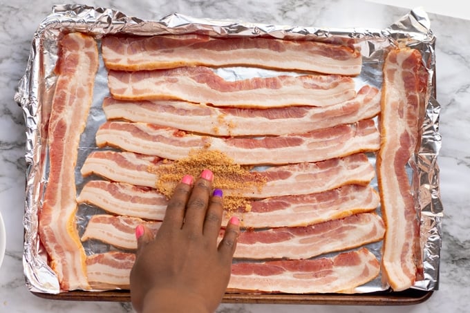 Pancetta stesa su una teglia con carta stagnola con la mano che mette lo zucchero di canna