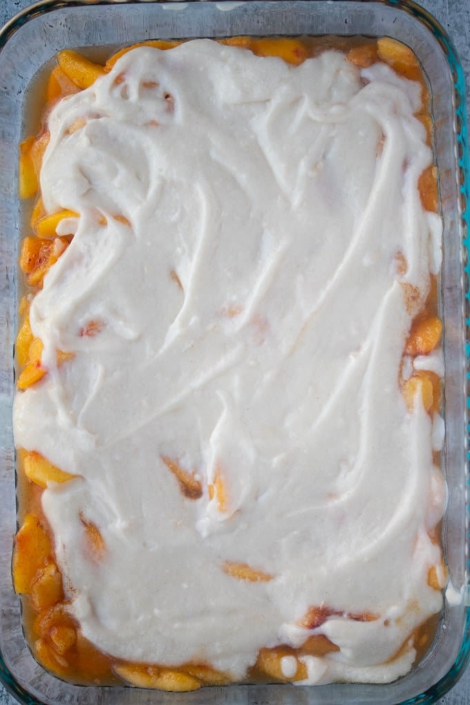 cake topping on peach cobbler in baking dish