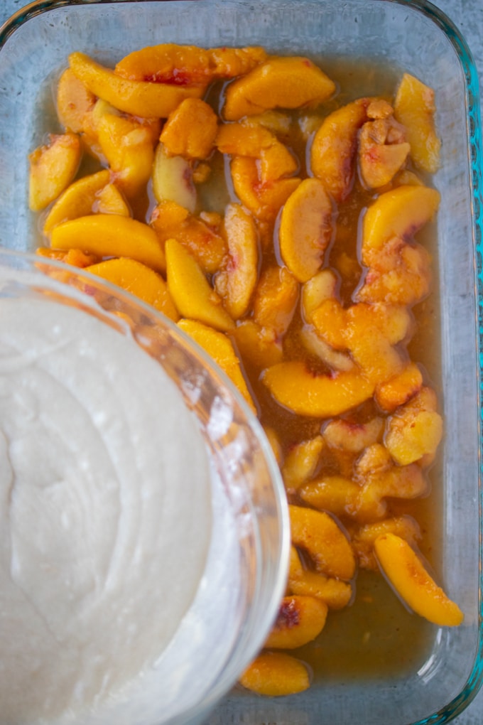 cake topping being poured over peaches in baking dish