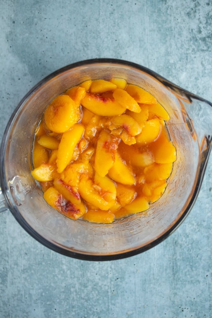 peaches with sugar, vanilla extract, and cinnamon in a glass bowl
