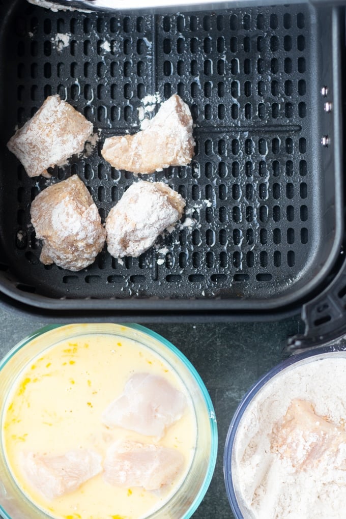 egg in a bowl, flour in a bowl, and air freyr basket with coated chicken in it