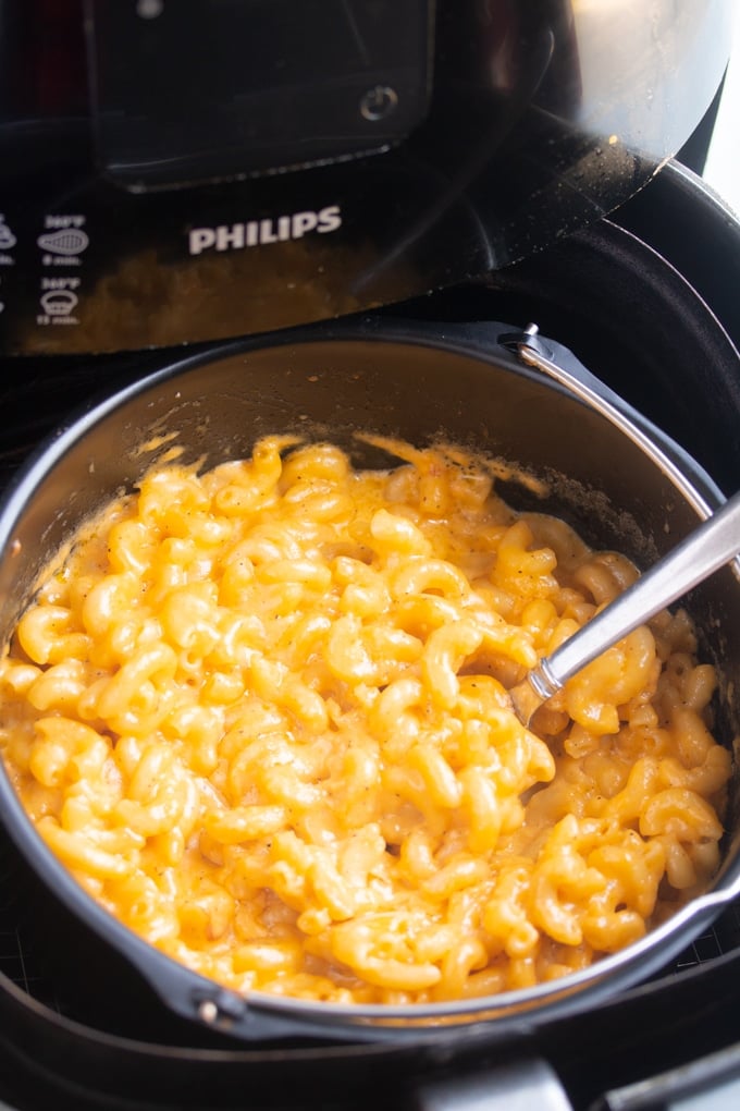 air fryer mac and cheese in the air fryer basket with a spoon sticking out