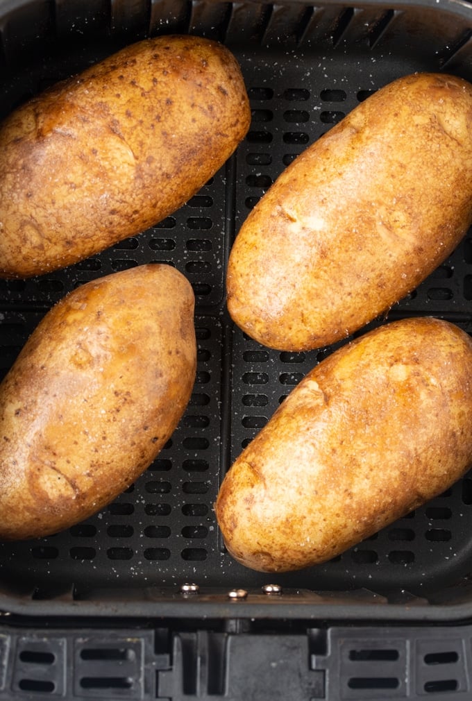 raw potatoes in air fryer basket with salt sprinkled on them