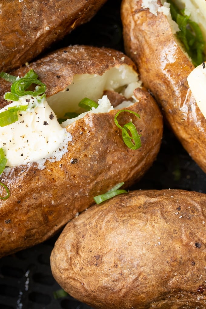 close up shot of air fryer baked potatoes with butter and green onion on top