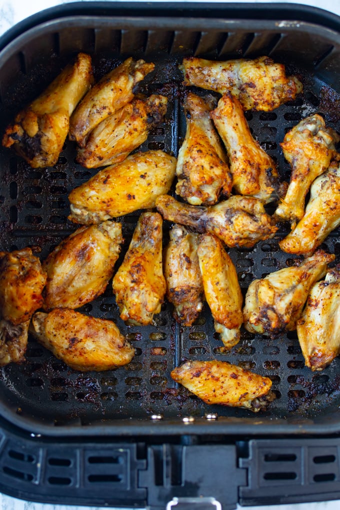 cooked chicken wings in air fryer basket with seasoning in it