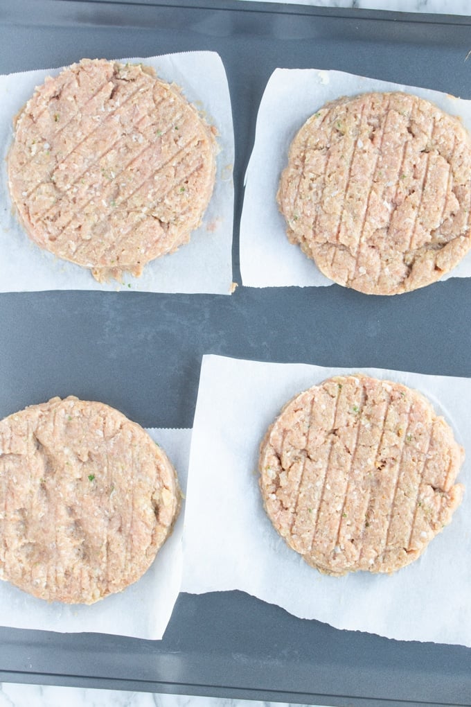 four raw turkey burgers laying on parchment paper