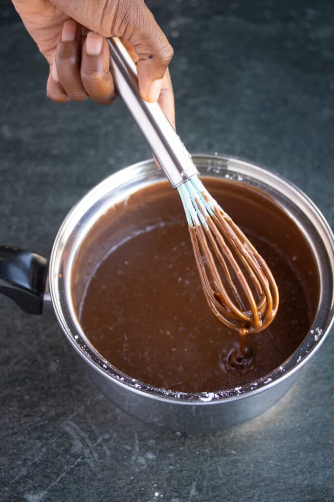 whisk with chocolate frosting dripping from it over sauce pan