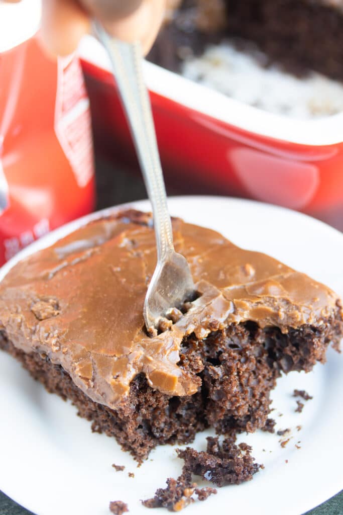 fork sticking out of piece of chocolate cola cake with crushed can and cake pan in background