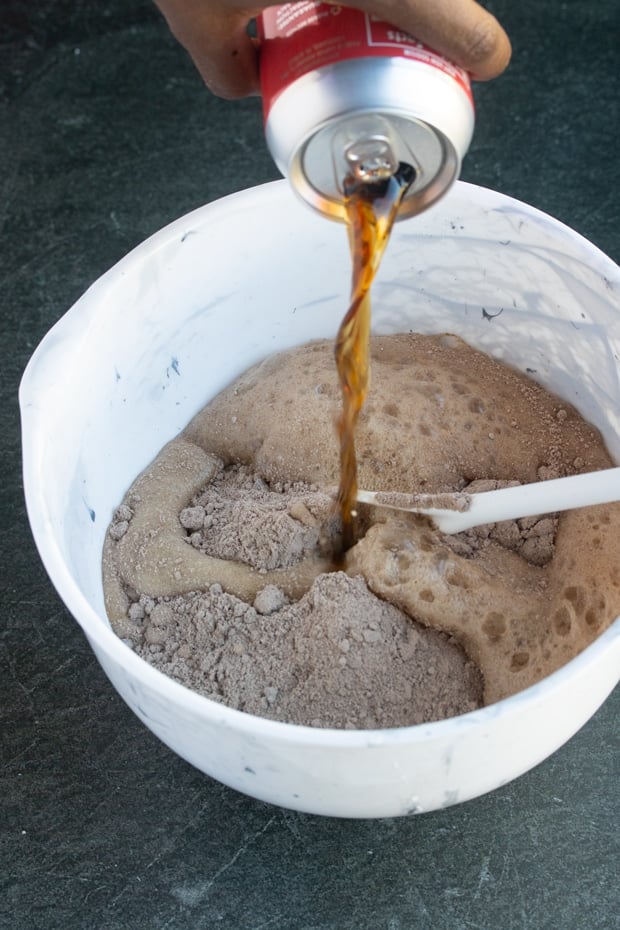 cola soda being poured into bowl with boxed caked mix