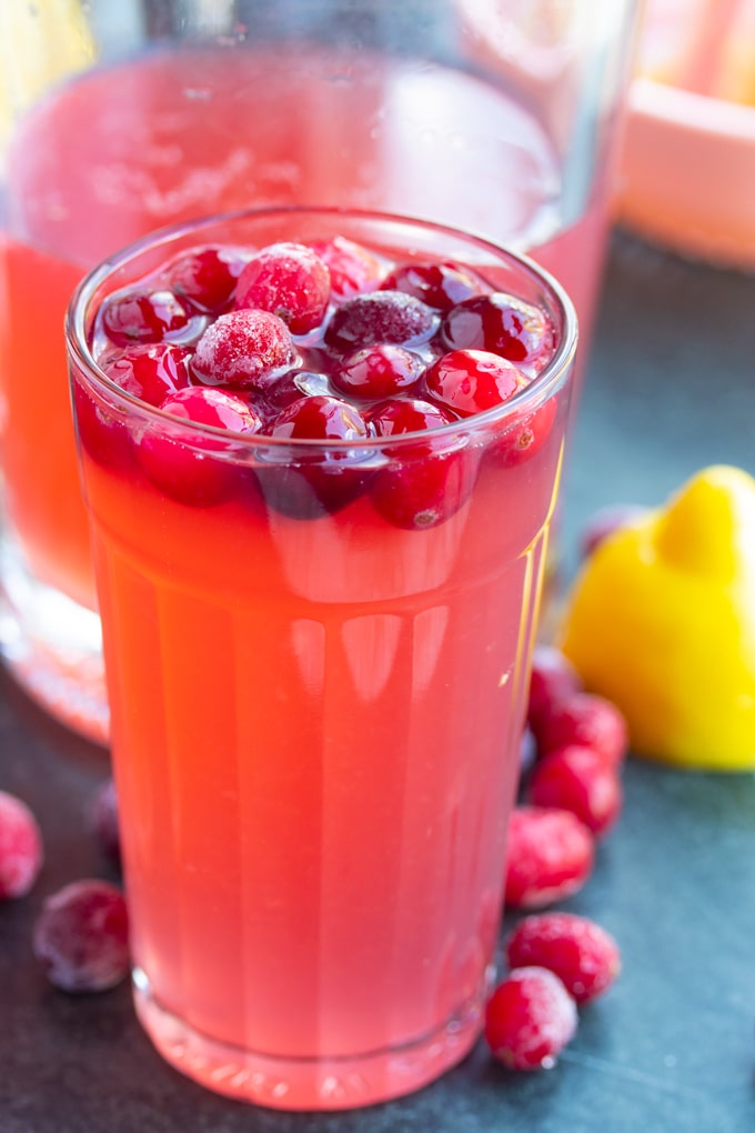 cranberry lemonade in glass with cranberries on top and around the glass