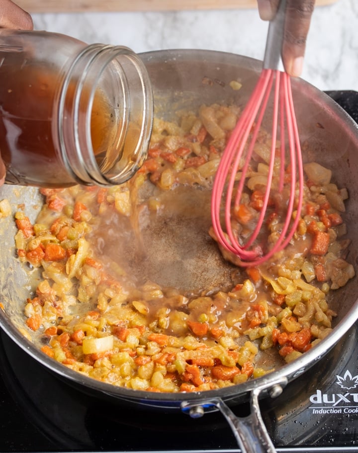 broth being poured into a skillet with whisk stirring