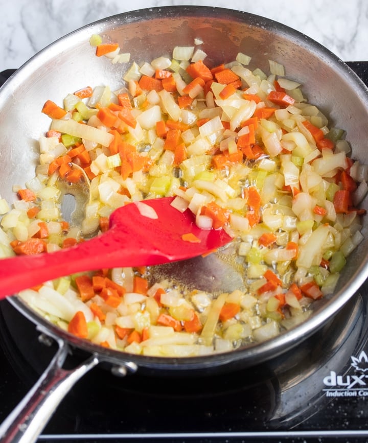 vegetables being softened in skillet with red silicone spatula